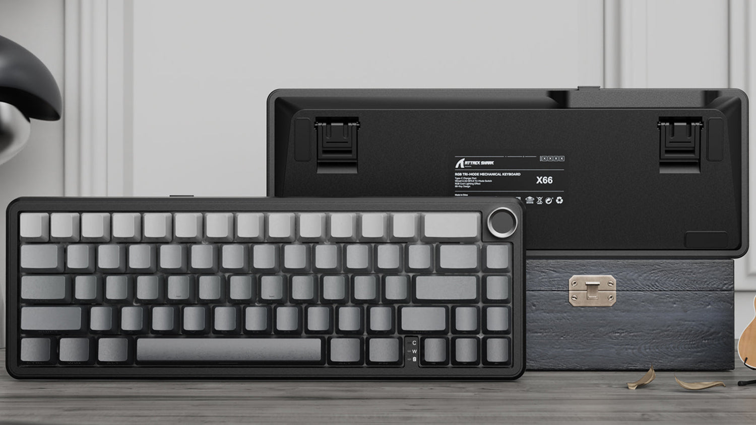 Front and back view of a grey mechanical keyboard with a knob, resting against a textured box.