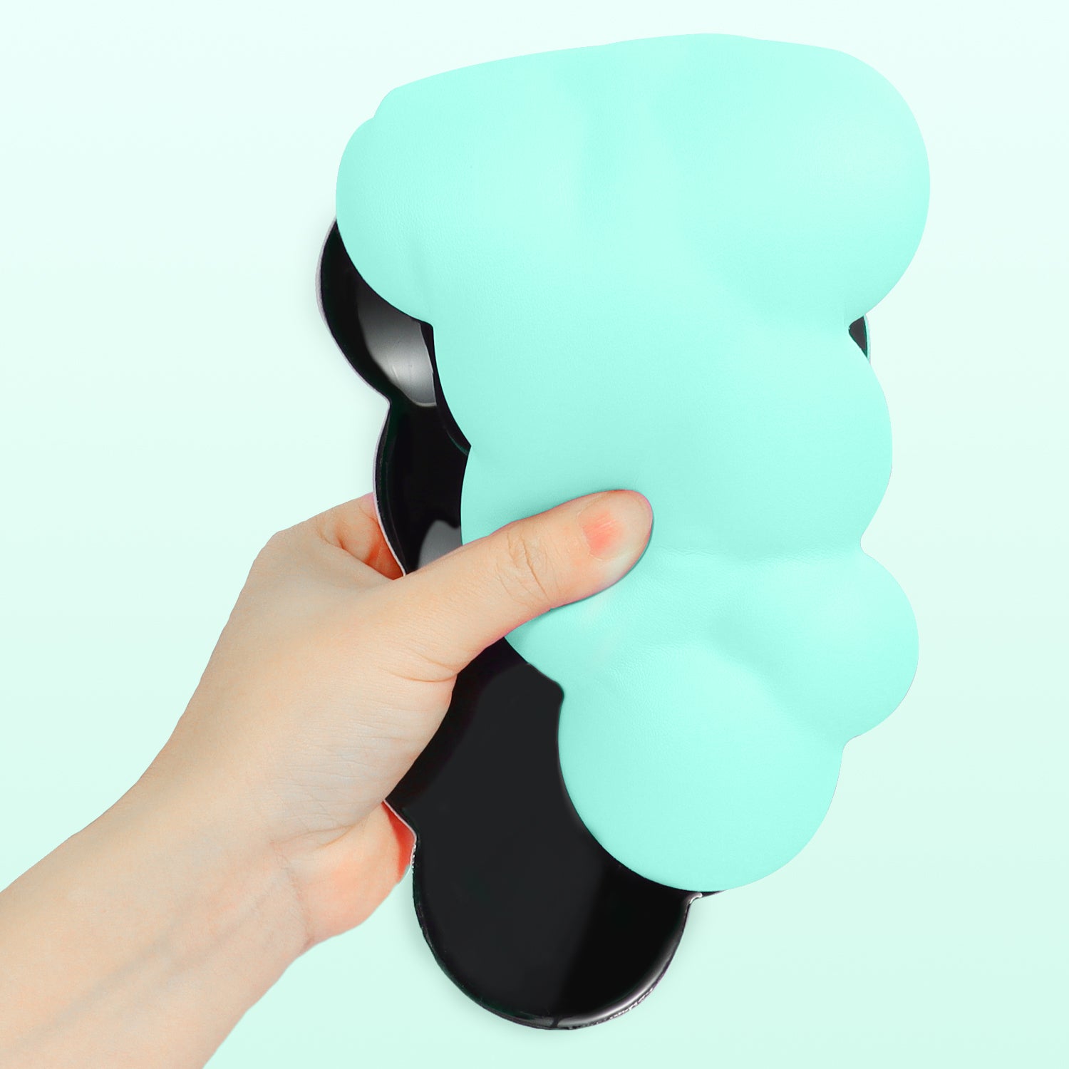 Hand holding mint green cloud-shaped wrist rest with black anti-slip base.