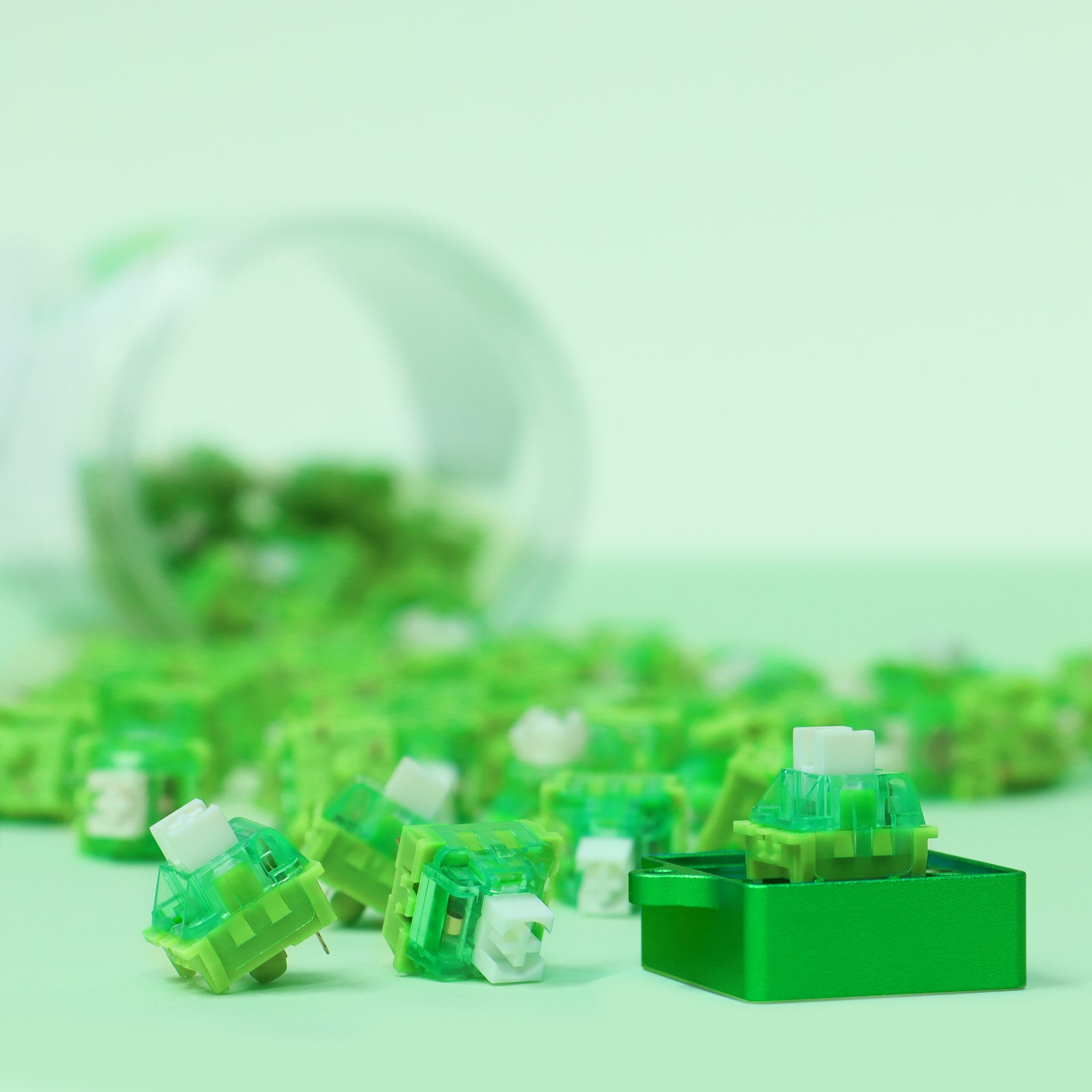 Assorted Jelly Green V3 mechanical keyboard switches on green surface with container.