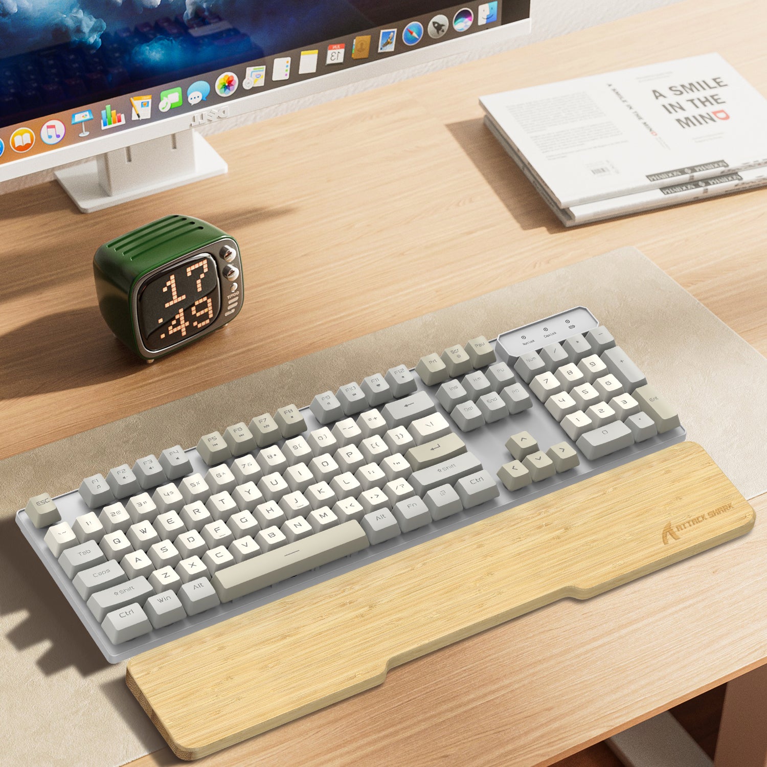 Bamboo wrist rest with cream and gray compact keyboard on light desk with clock.